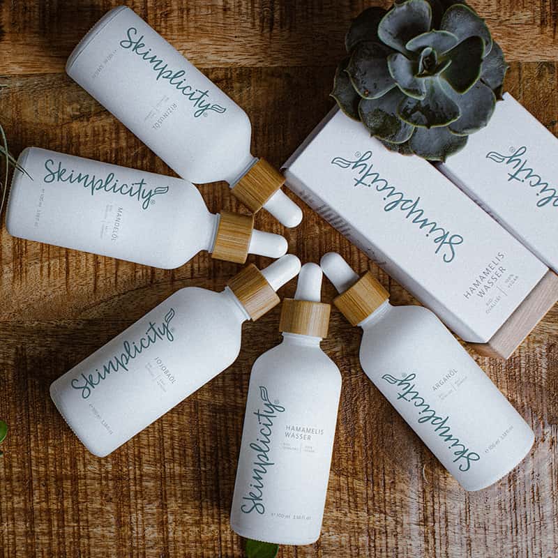 Alle Skinplicity Öle als Blume gefächert auf Holz-Untergrund